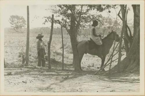 Woman on horseback with man to the left