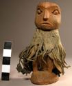 Wooden effigy of man, wearing fringed leather cape with tinklers
