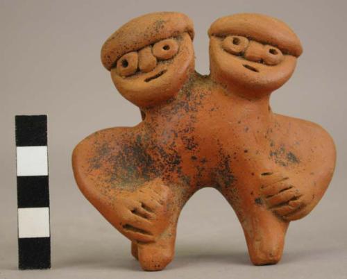 Double-headed figurine with suspension holes and traces of black paint.