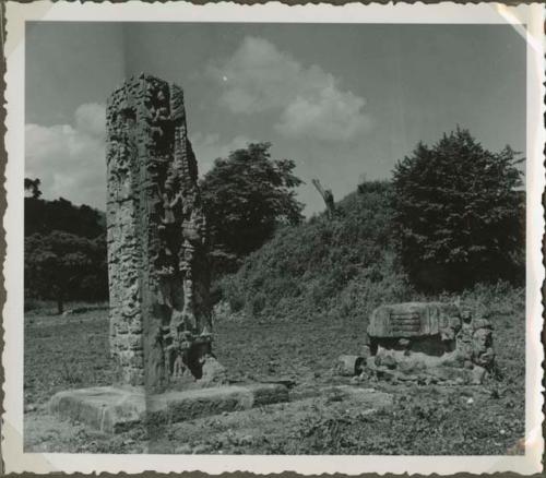 Upright stela and large stone sculpture in an open field