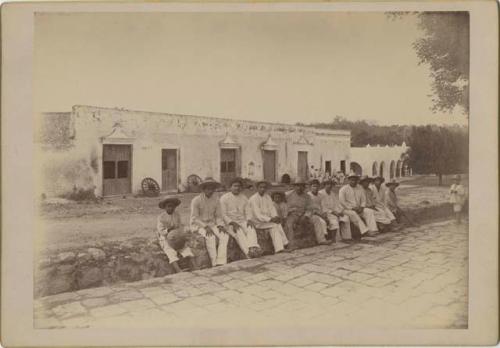 Men and boys seated on a curb outside a building