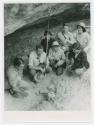 Hallam Movius, Jr. squatting, looking at skull at excavation site with 6 people gathered around him.