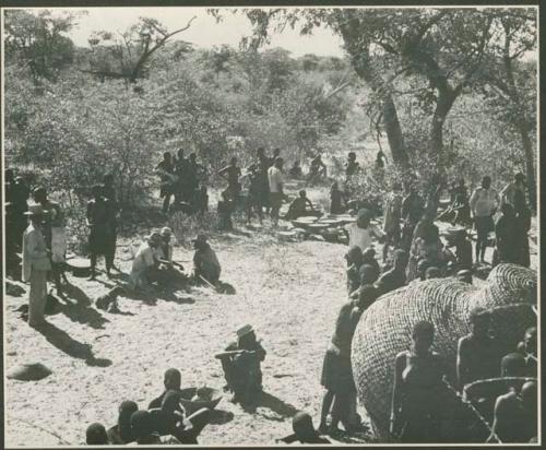 Group of people sitting and standing outside kraal (print is a cropped image)