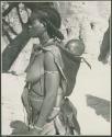 Woman carrying a baby on her back, with baobab tree in background (print is a cropped image)