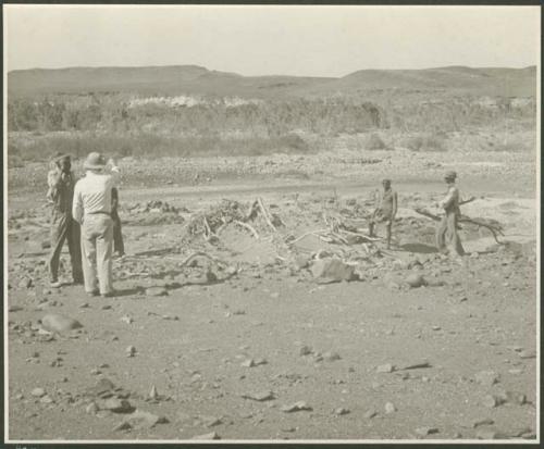 Five men standing, and one pointing (print is a cropped image)