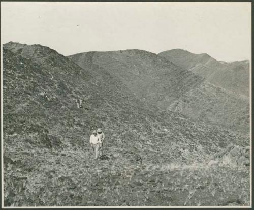 Men descending a hill (print is a cropped image)