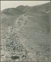 Person walking on side of hill; hill shows tipped strata (print is a cropped image)