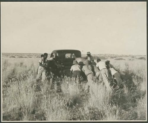 Men pushing an expedition truck (print is a cropped image)