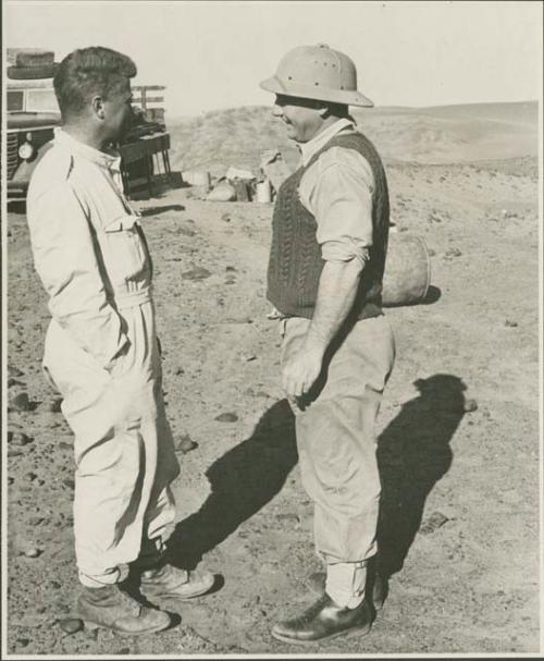 Two expedition members standing, with a truck in the background (print is a cropped image)