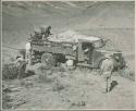 Expedition members putting brush under wheels of truck and retrieving something from the load (print is a cropped image)