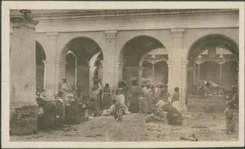 Group of people standing or sitting under an arched building, possibly Antigua