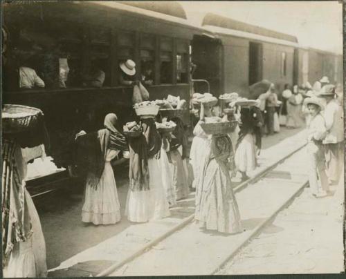 Women holding baskets next to train, possibly Zacapa