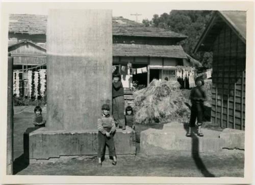 Children next to stone monument, with house in background