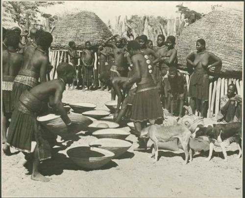 Group of people working with baskets of grain, with dogs next to them (print is a cropped image)