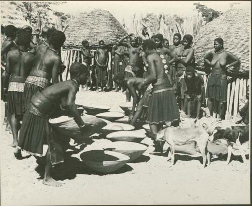 Group of people working with baskets of grain, with dogs next to them (print is a cropped image)