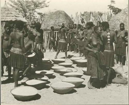 Group of people working with baskets of grain, with dogs next to them (print is a cropped image)