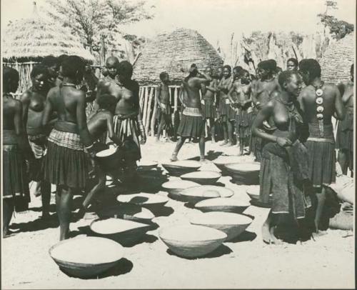 Group of people working with baskets of grain, with dogs next to them (print is a cropped image)