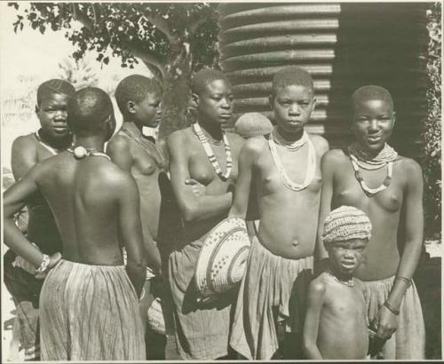 Group of women and children standing, one woman holding a basket (print is a cropped image)