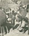 People standing near grain storage baskets (print is a cropped image)