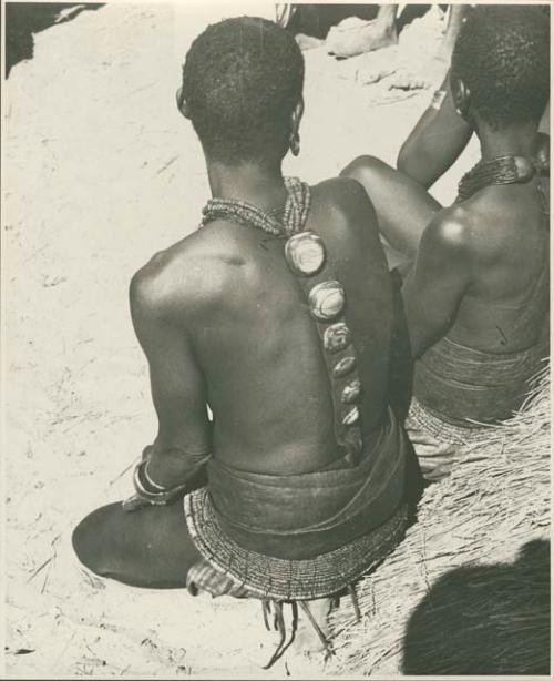 Woman sitting with her back to the camera, wearing ornaments (print is a cropped image)