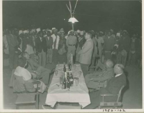 Group of people standing and listening to an expedition member, with other expedition members sitting at a table