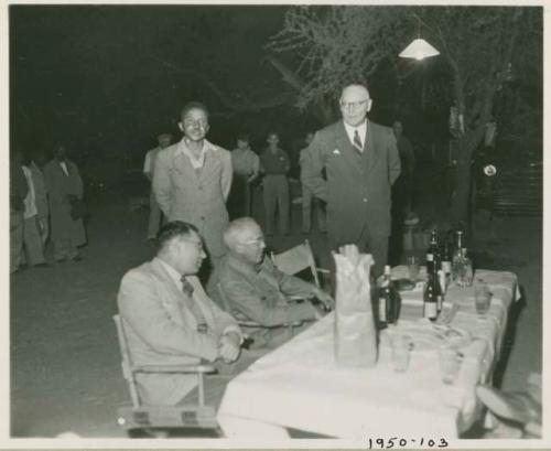 Group of people standing behind expedition members sitting at a table