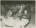 Colonel Hoogenhout, Laurence Marshall, John Neser, others seated around table, large crowd of people behind