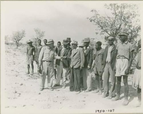 Group of people standing and talking with William Hartley, Edward Hartley and Laurence Marshall, holding a camera