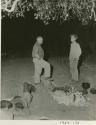 Man reclining next to Laurence Marshall and John Marshall standing in the expedition camp