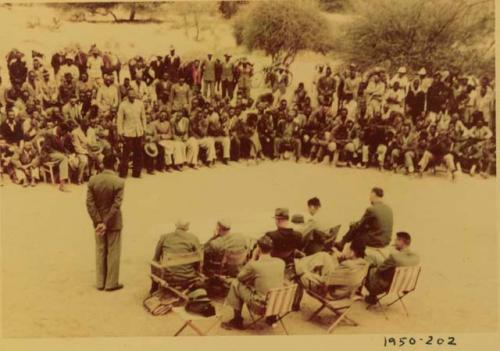 Indaba at Omajetti, Herero chief, with a large group of people sitting and standing behind him, addressing expedition members, including Colonel Hoogenhout, John Neser, Laurence Marshall and John Marshall