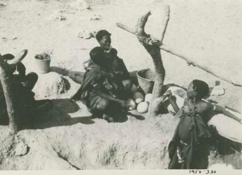 Group of women sitting next to a well, with ostrich egg shells on the ground next to them