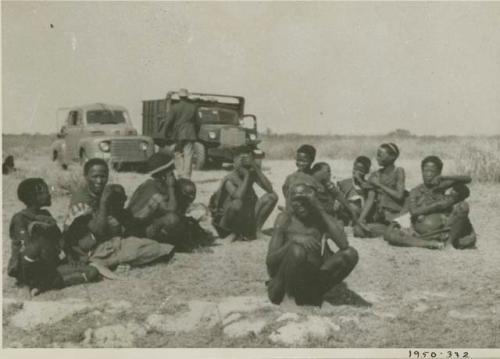 Group of people sitting, the first group that the expedition encountered, with expedition trucks in the background