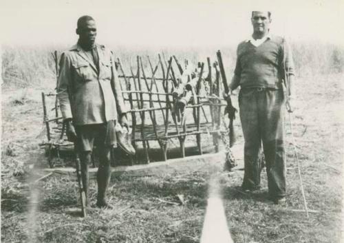 Two men standing next to a "sled"