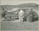 Expedition members standing and looking at the truck, with brush under the wheels, at the crest of a hill (print is a cropped image)