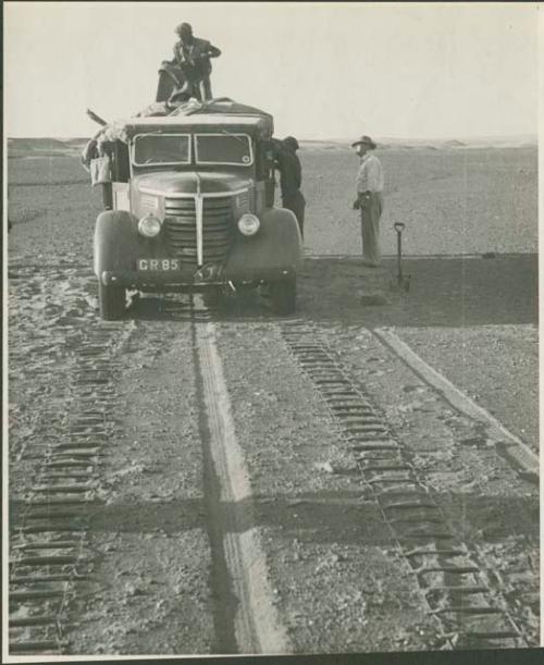 Expedition members standing on and next to truck, and chains laid out ahead of wheels (print is a cropped image)