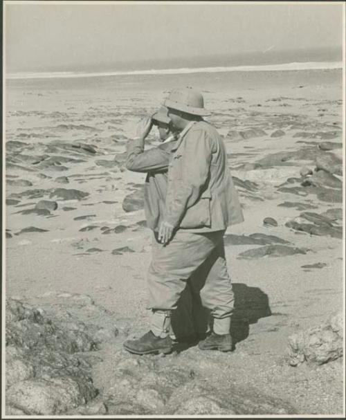 Two expedition members standing on beach looking at water (print is a cropped image)