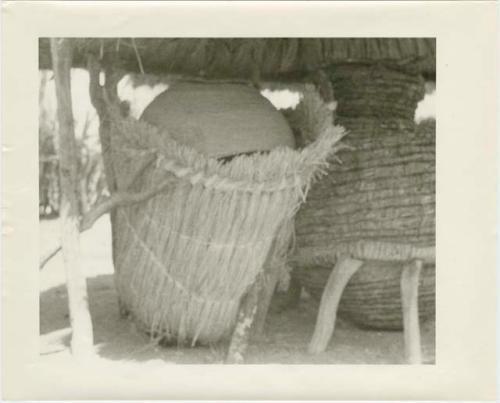 Two storage baskets under a thatched roof (print is a cropped image)