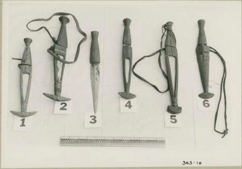 Six knives, five of them in sheathes, with a ruler for measurement (print is a cropped image)