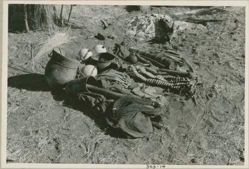 "Gao Medicine's" possessions, including rattles, oracle disks, an Ovambo pot, ostrich egg shells, quiver, and cord; ashes from a fire in the background