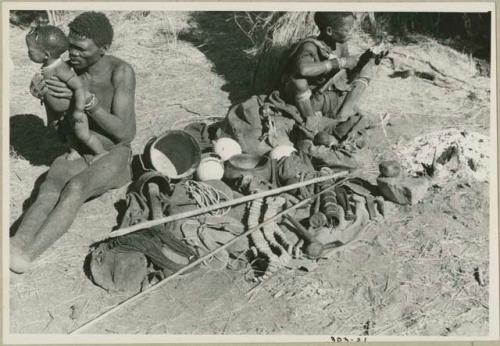 "Gao Medicine" holding his son, /Gaishay, and his wife, Di!ai, nearby; "Gao Medicine's" possessions are laid between them with a skerm in the background