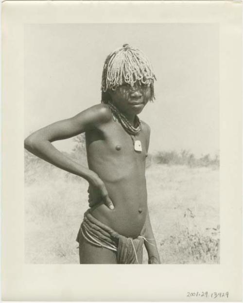 Girl wearing beads in her hair, standing (print is a cropped image)