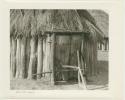 Hut built of wooden poles and a thatched roof; the door is locked with a forked, wooden pole (print is a cropped image)
