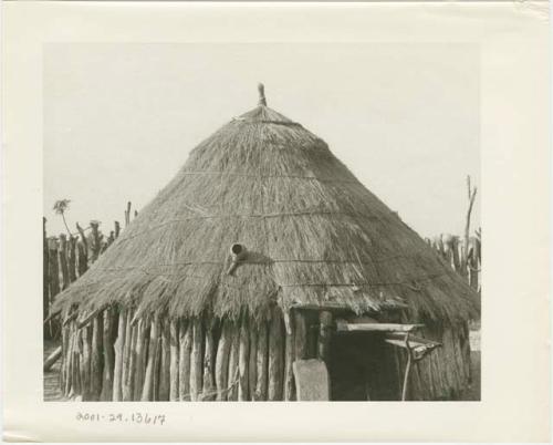 Hut with a thatched roof tied with cord (print is a cropped image)