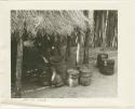 Wooden milk buckets and a funnel in front of a hut, inside a kraal (print is a cropped image)
