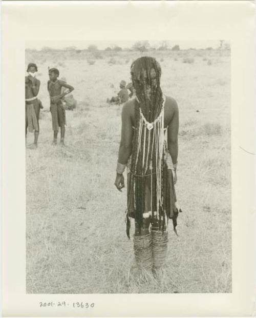 Girl standing, seen from behind, with other people in the background (print is a cropped image)