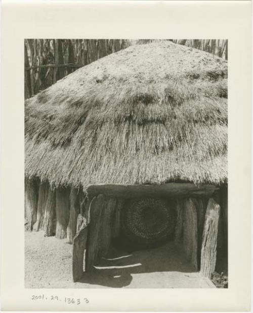 Hut with a basket in the entrance (print is a cropped image)