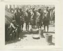 Women and children by a hut with mortars and baskets by their feet (print is a cropped image)