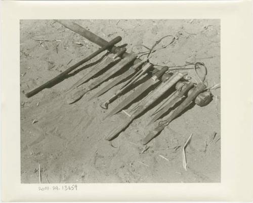 Four knives, their wooden sheaths, and a stick, all lying on a pestle (print is a cropped image)
