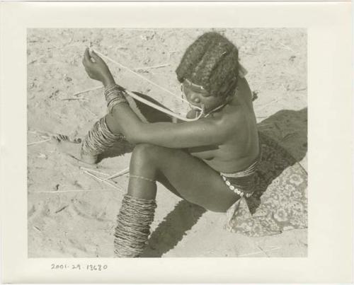 Girl sitting and playing a musical bow (print is a cropped image)