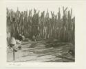 Baskets, pots, and a chicken by a kraal fence (print is a cropped image)